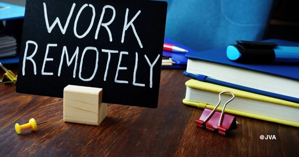 Papan tulis bertuliskan Work Remotely di atas meja kerja sebagai ilustrasi sistem kerja virtual assistant jarak jauh dari JasaVirtualAssistantID.
