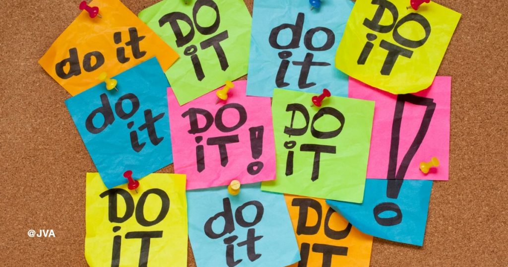 Tumpukan catatan post-it berwarna-warni bertuliskan 'Do It' yang menumpuk di papan buletin, melambangkan kewalahan operasional dan tanda bisnis butuh virtual assistant untuk delegasi tugas.