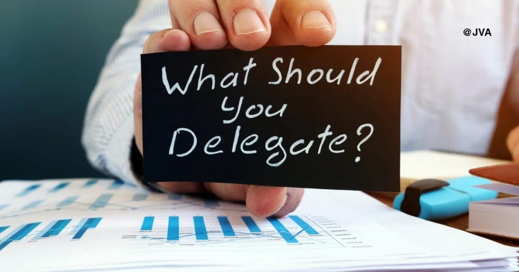 Seorang pria memegang kartu bertuliskan "What Should You Delegate?" untuk persiapan rekrut Virtual Assistant.